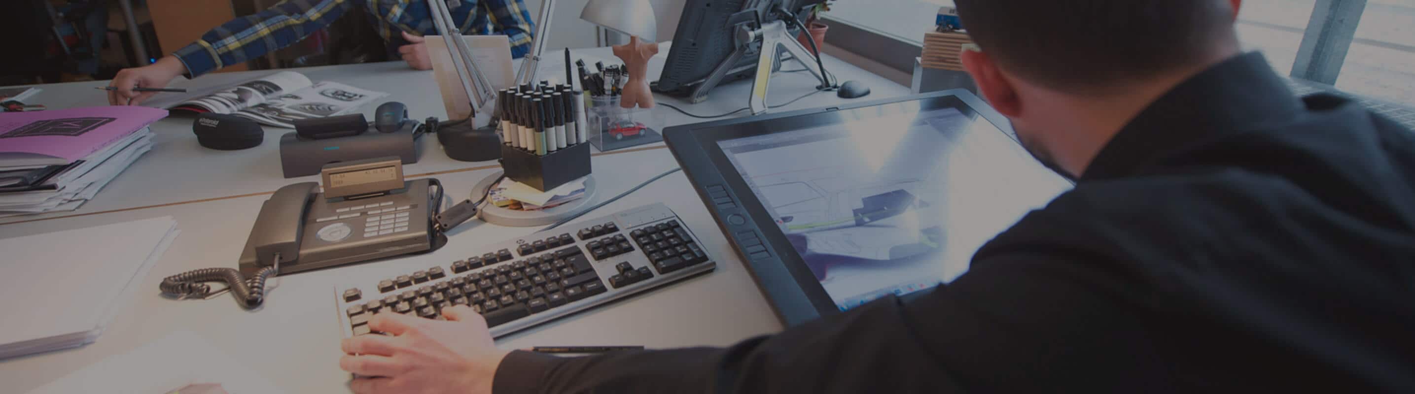 View behind a deak worker’s shoulder with a smart tablet on the desk – SEAT Human Resources View behind a deak worker’s shoulder with a smart tablet on the desk – SEAT Human Resources